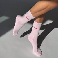 Pink socks with red logo worn by a person on a gray background